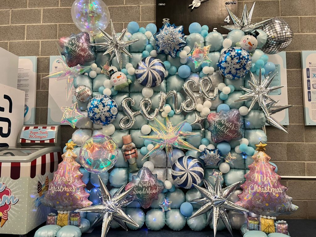 Large balloon wall backdrop with foil stars, Christmas trees, and snowflakes for corporate festive event in South Yorkshire