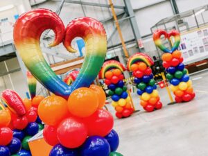 Professional balloon columns with rainbow heart toppers installed at an Amazon warehouse using air-filled, CE certified balloons