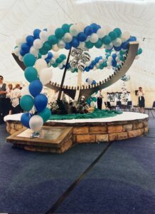 Suspended balloon garland in Sheffield International Venues colours above the statue to the birth of stainless steel, with silver foil balloon bouquets printed with the SIV logo, built for the Rolling Stones concert at Don Valley Stadium, July 1995