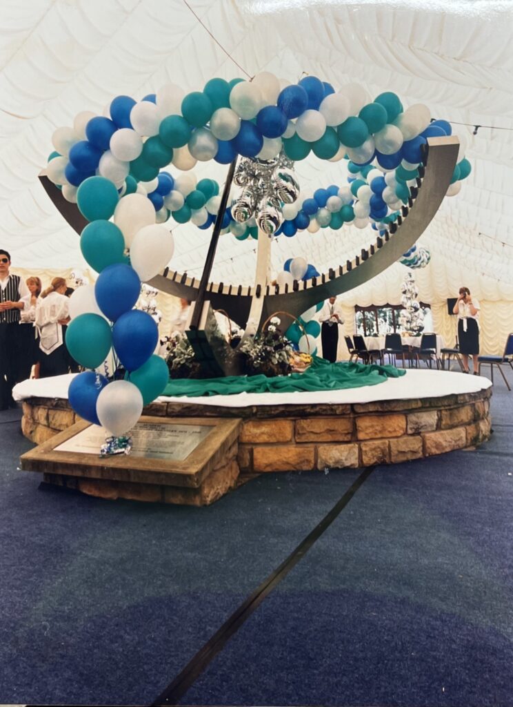 Suspended balloon garland in Sheffield International Venues colours above the statue to the birth of stainless steel, with silver foil balloon bouquets printed with the SIV logo, built for the Rolling Stones concert at Don Valley Stadium, July 1995